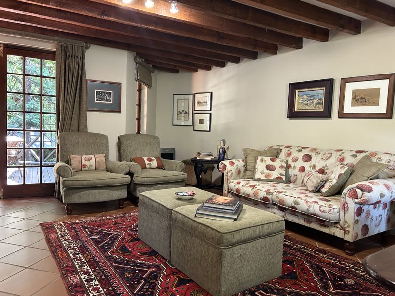 A cozy living room featuring exposed timber ceiling beams, terracotta floor tiles, and direct access to an outdoor patio through classic french doors.
