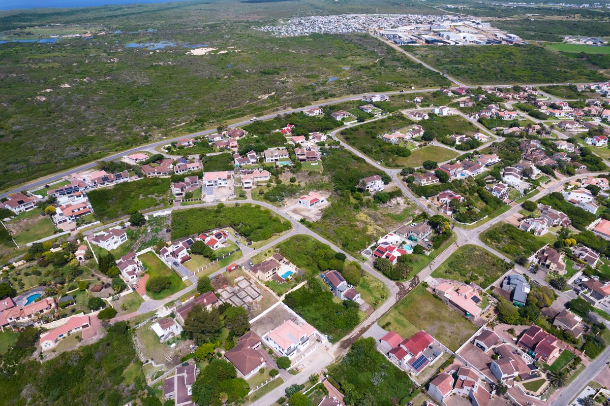 An aerial view of a residential estate featuring established homes, paved road infrastructure, and surrounding coastal landscape.