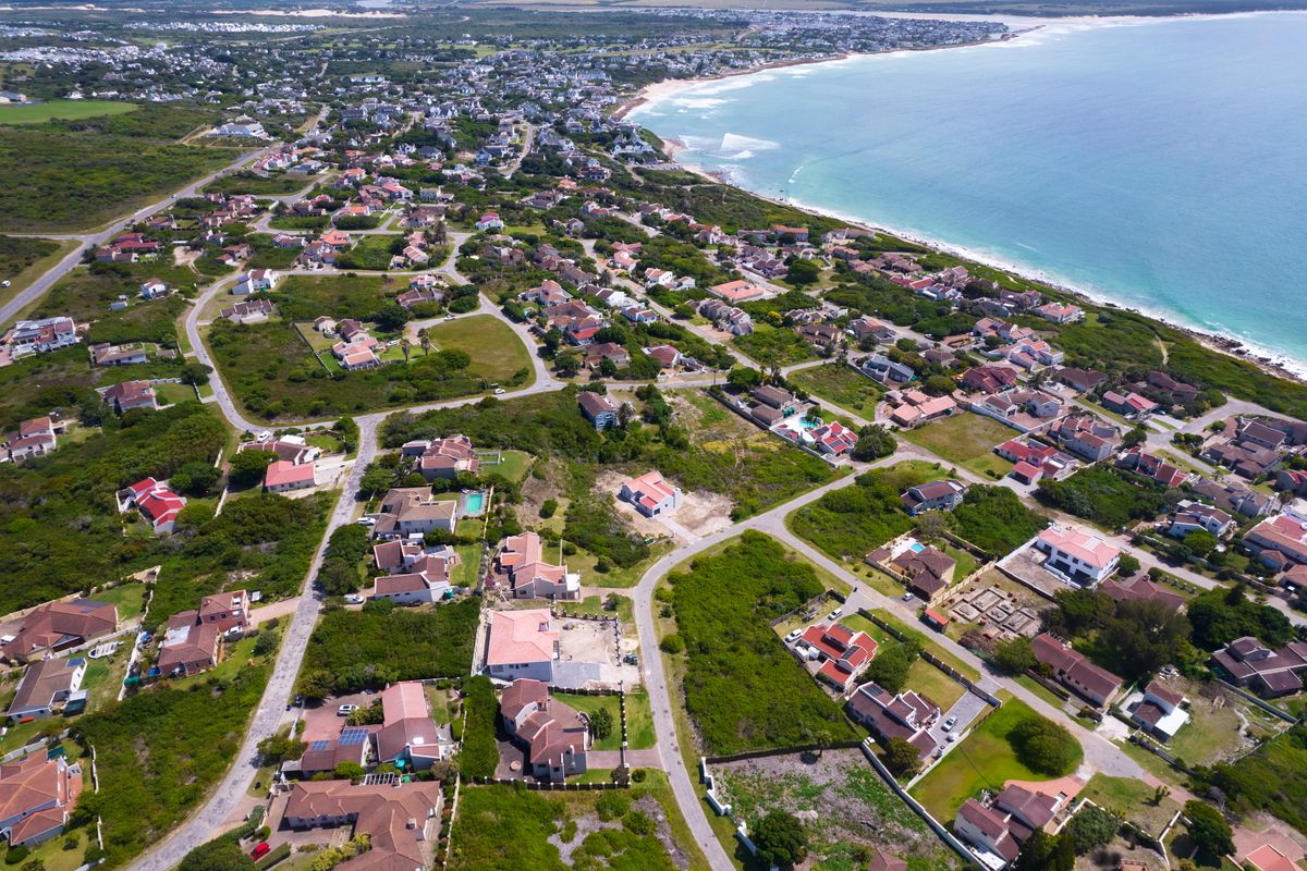 An aerial view of a coastal residential neighborhood, showcasing the surrounding landscape, street layout, and proximity to the ocean.