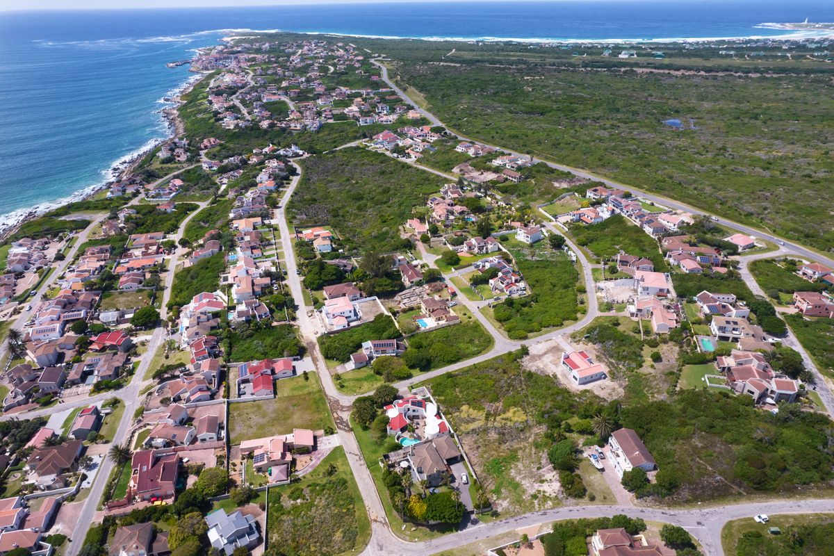 An aerial view of a coastal residential estate, showcasing the surrounding landscape, road infrastructure, and proximity to the ocean.