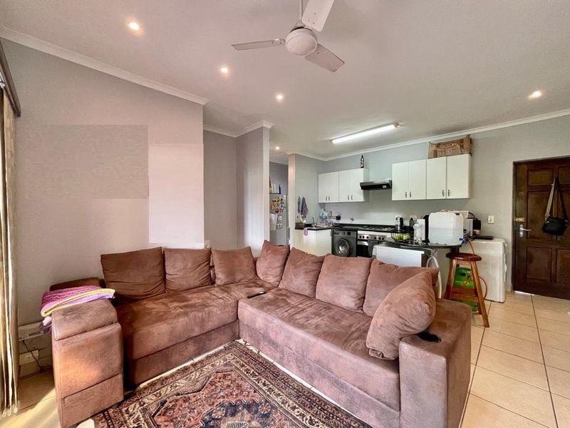 Open-plan living area featuring a functional kitchen with built-in cabinetry, extractor fan, and tiled flooring throughout the combined space.