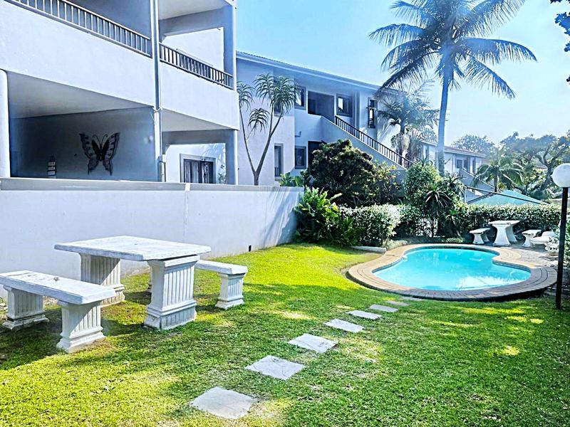 A well-maintained communal garden area featuring a swimming pool, paved pathways, and access to the apartment building's balconies and exterior staircases.
