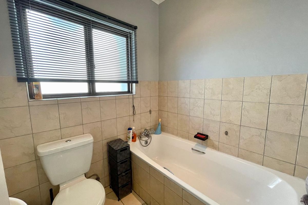 A functional bathroom featuring a bathtub with mixer tap, a toilet, and neutral wall tiling with a window providing natural light.