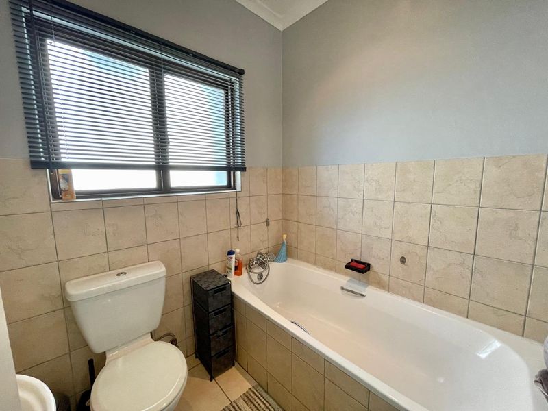 A functional bathroom featuring a bathtub with mixer tap, a toilet, and neutral wall tiling with a window providing natural light.
