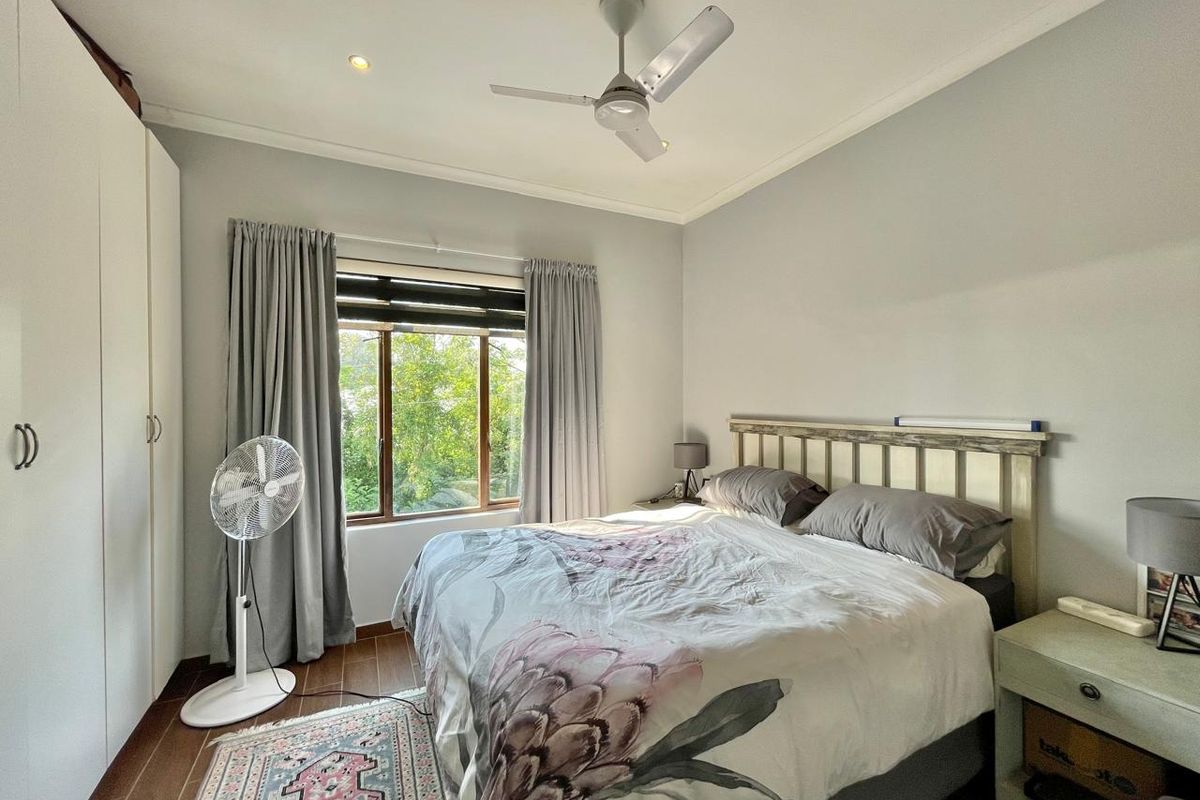 A well-maintained bedroom featuring built-in cupboards, a ceiling fan, recessed lighting, and timber-look flooring with a pleasant garden view.