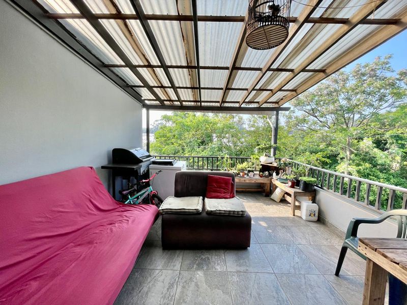 Covered balcony featuring tiled flooring and metal railings, offering an outdoor space with a leafy outlook.