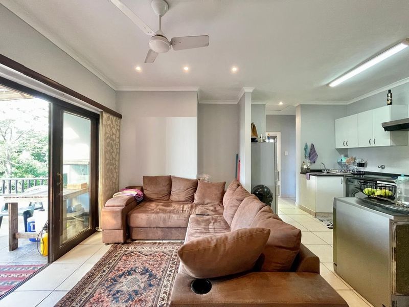 Open-plan living area featuring tiled floors, recessed lighting, and a functional kitchen with cabinetry, flowing seamlessly to an outdoor patio through sliding glass doors.