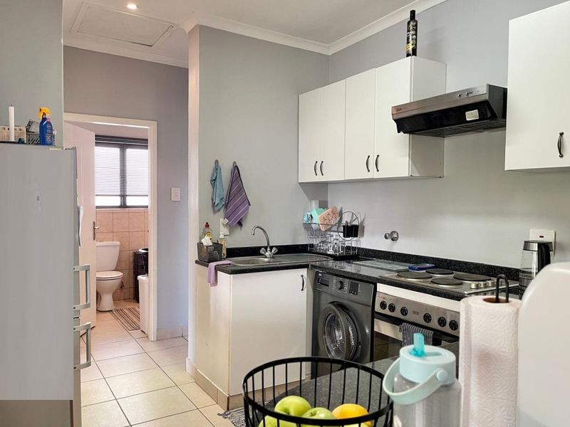 Compact kitchen featuring white cabinetry, granite countertops, integrated electric hob and oven, and tiled flooring, with direct access to an adjacent bathroom.