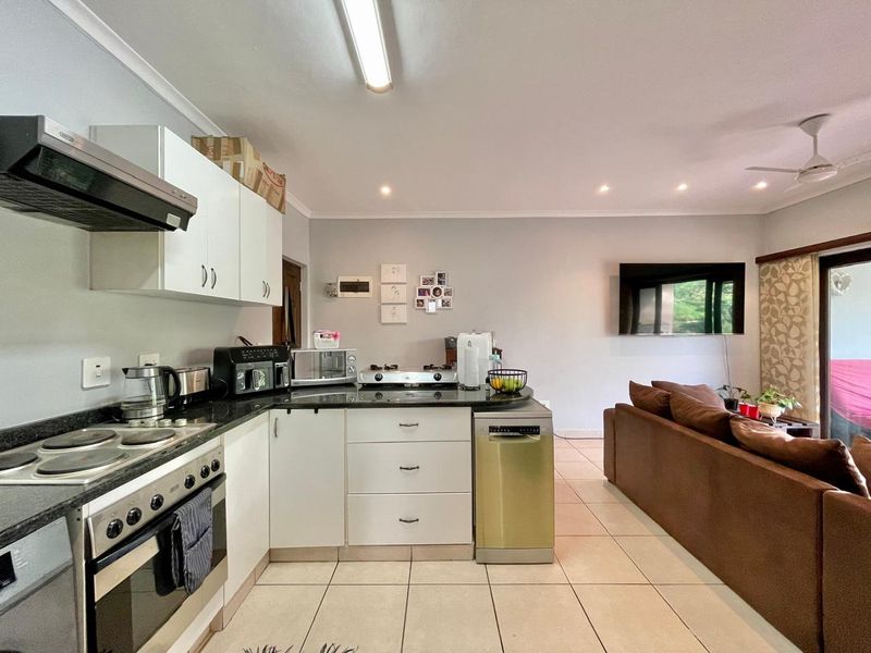 Open-plan kitchen and living area featuring tiled flooring, granite countertops, built-in cabinetry, and integrated kitchen appliances, creating a functional and connected living space.