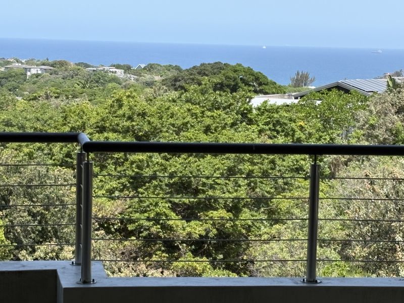 A scenic elevated view overlooking lush coastal greenery and the ocean, framed by a modern stainless steel and cable balcony railing.