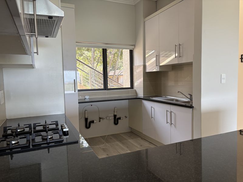 Modern kitchen featuring granite countertops, gas hob, extractor fan, and white cabinetry, with an open space prepared for under-counter appliance installation.