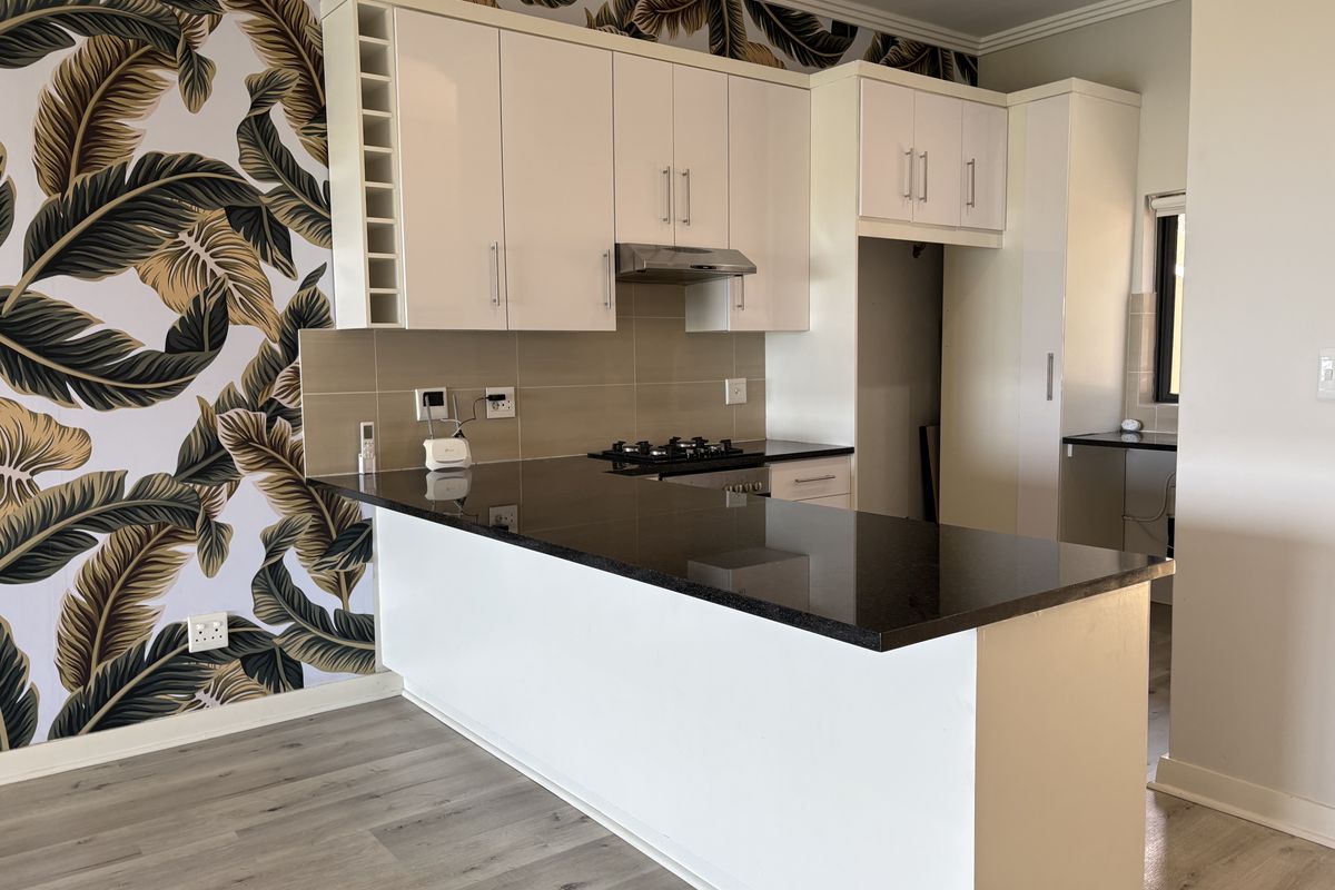 Modern kitchen featuring white cabinetry, dark granite countertops, gas hob, extractor fan, and stylish patterned wallpaper, offering a clean and functional cooking space.