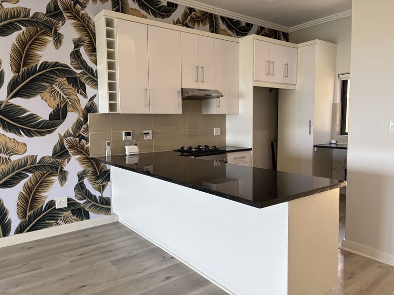 Modern kitchen featuring white cabinetry, dark granite countertops, gas hob, extractor fan, and stylish patterned wallpaper, offering a clean and functional cooking space.