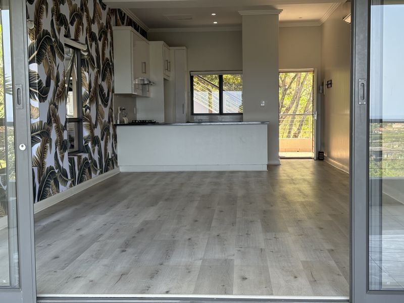 Spacious open-plan living and kitchen area featuring modern laminate flooring, built-in cabinetry, and large sliding glass doors leading to an outdoor space.