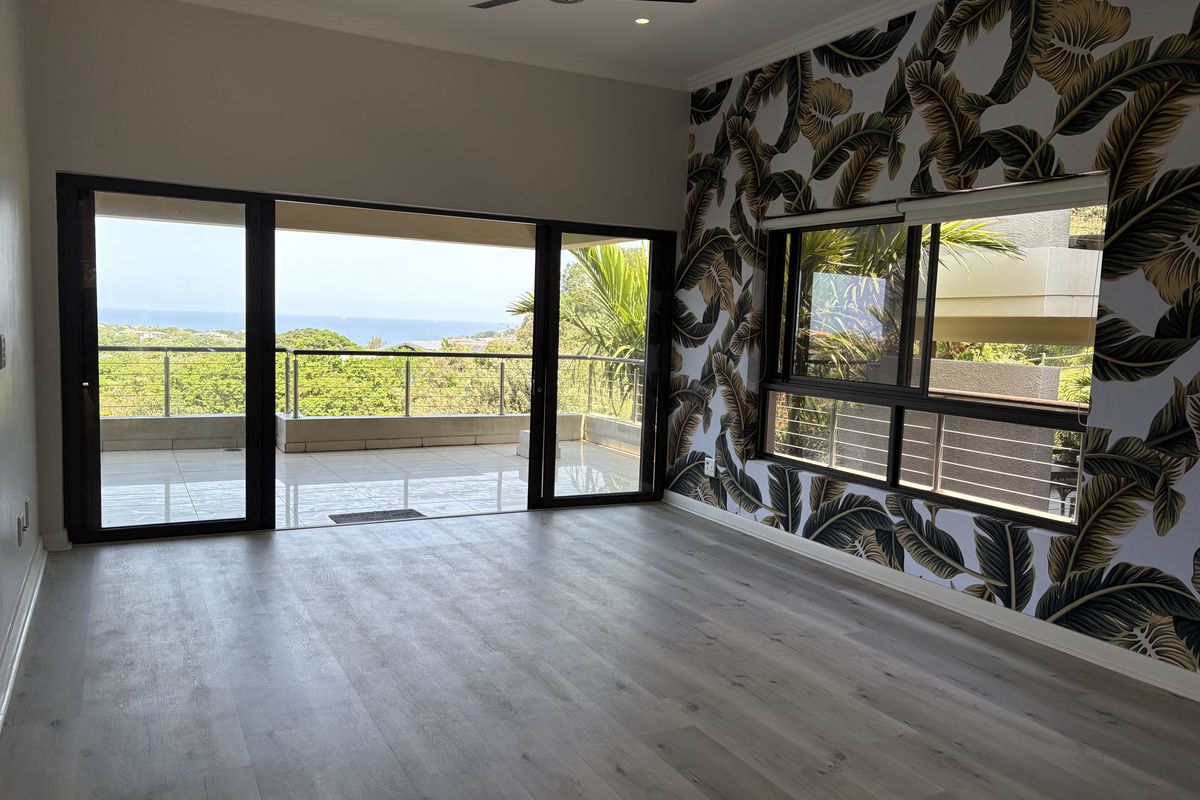 Spacious living area featuring modern laminate flooring, a striking feature wall, and large sliding doors opening onto a balcony with scenic coastal views.