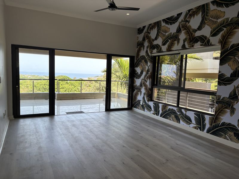 Spacious living area featuring modern laminate flooring, a striking feature wall, and large sliding doors opening onto a balcony with scenic coastal views.