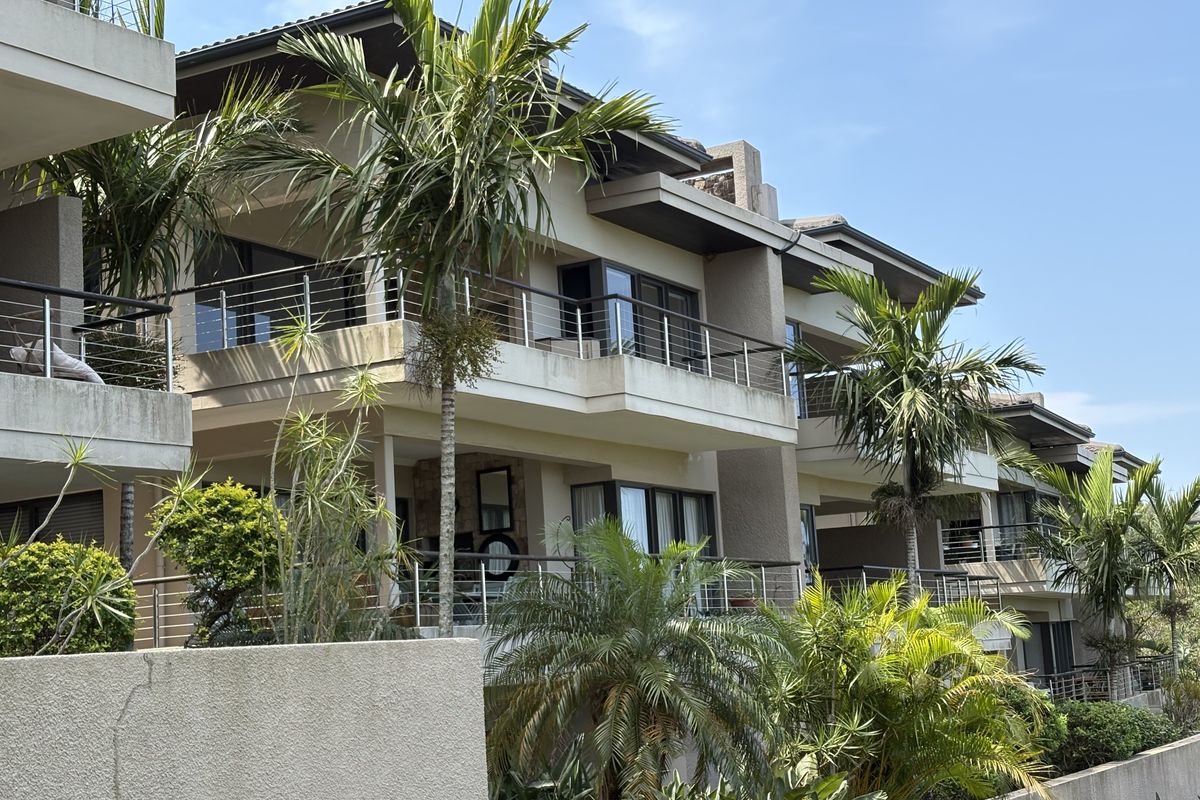 A view of the rear elevation of a modern apartment complex featuring multiple balconies with stainless steel railings and landscaped garden areas.