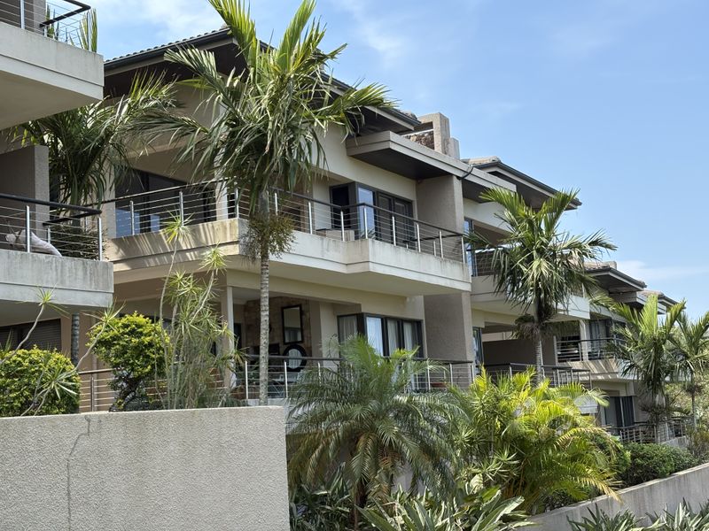 A view of the rear elevation of a modern apartment complex featuring multiple balconies with stainless steel railings and landscaped garden areas.