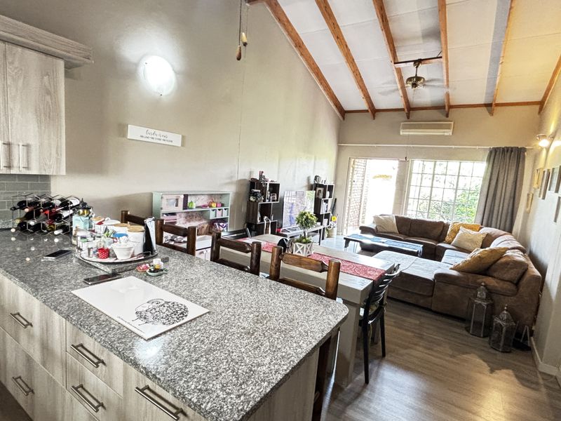 Open-plan living area featuring a modern kitchen with granite countertops, exposed timber ceiling beams, and laminate flooring, creating a spacious and functional living environment.