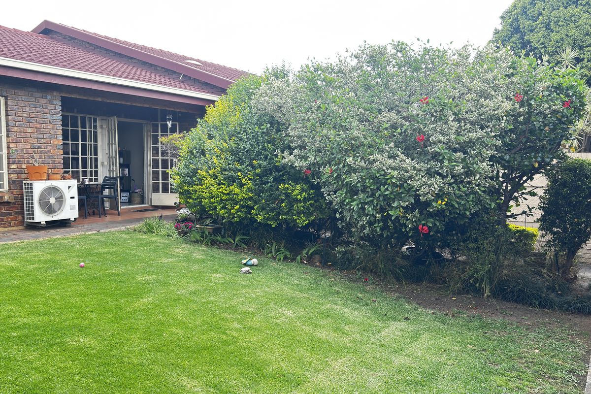 Rear view of the townhouse featuring a brick facade, tiled roof, a well-maintained lawn, and a paved patio area with established garden landscaping.