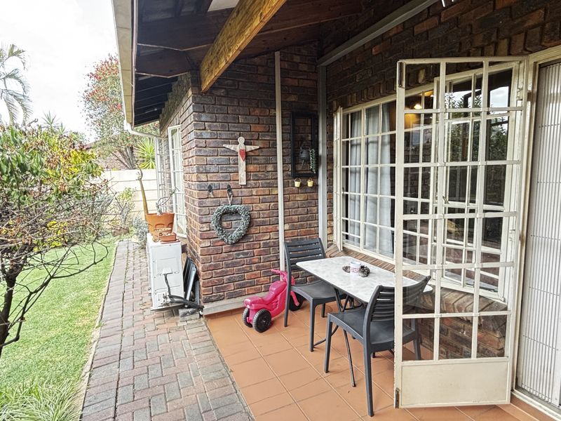 A covered patio area featuring exposed brick walls, tiled flooring, and a timber roof beam, providing direct access to the garden.