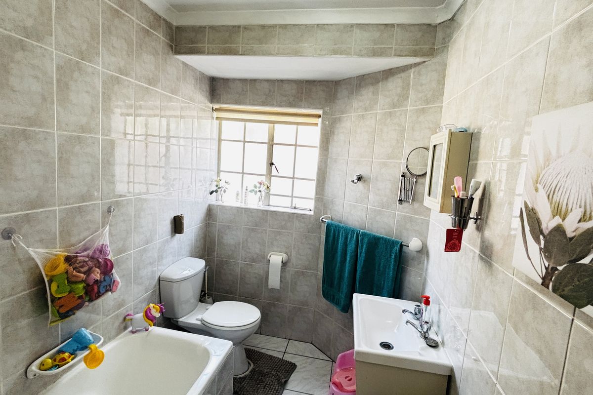 A functional bathroom featuring fully tiled walls and floors, a standard bathtub, a pedestal basin, and a toilet with natural light from a window.