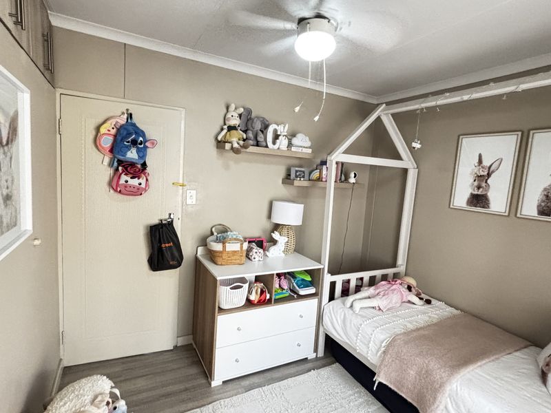 A well-maintained bedroom featuring neutral wall tones, laminate flooring, built-in storage cupboards, and a functional ceiling fan.