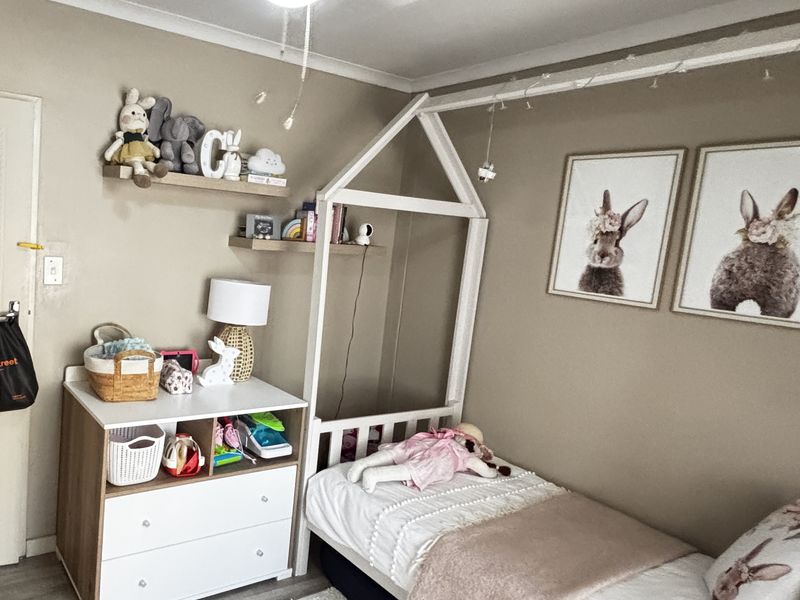A cozy bedroom featuring neutral wall tones, built-in shelving, and a functional layout suitable for a child's room.