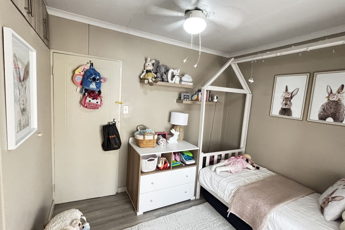 A well-maintained bedroom featuring neutral wall tones, laminate flooring, built-in storage cupboards, and a functional ceiling fan.