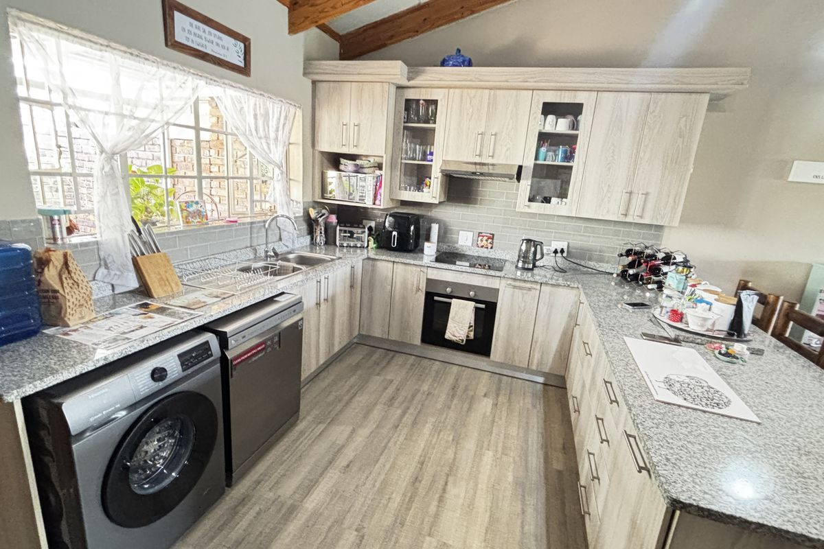 A functional kitchen featuring light wood-grain cabinetry, granite countertops, built-in oven with hob, and exposed timber ceiling beams, offering a practical workspace.