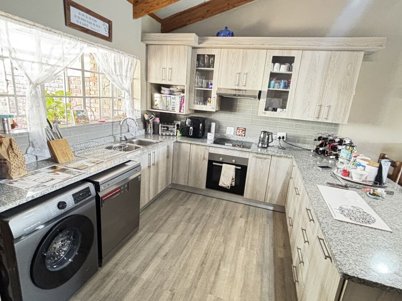A functional kitchen featuring light wood-grain cabinetry, granite countertops, built-in oven with hob, and exposed timber ceiling beams, offering a practical workspace.