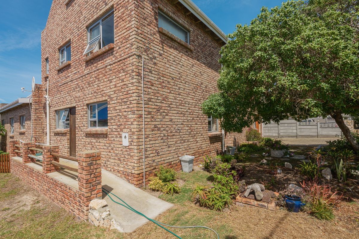 Rear view of a double-story face brick house featuring a concrete access ramp, brick boundary wall, and established garden area.