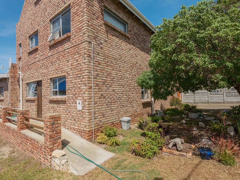 Rear view of a double-story face brick house featuring a concrete access ramp, brick boundary wall, and established garden area.