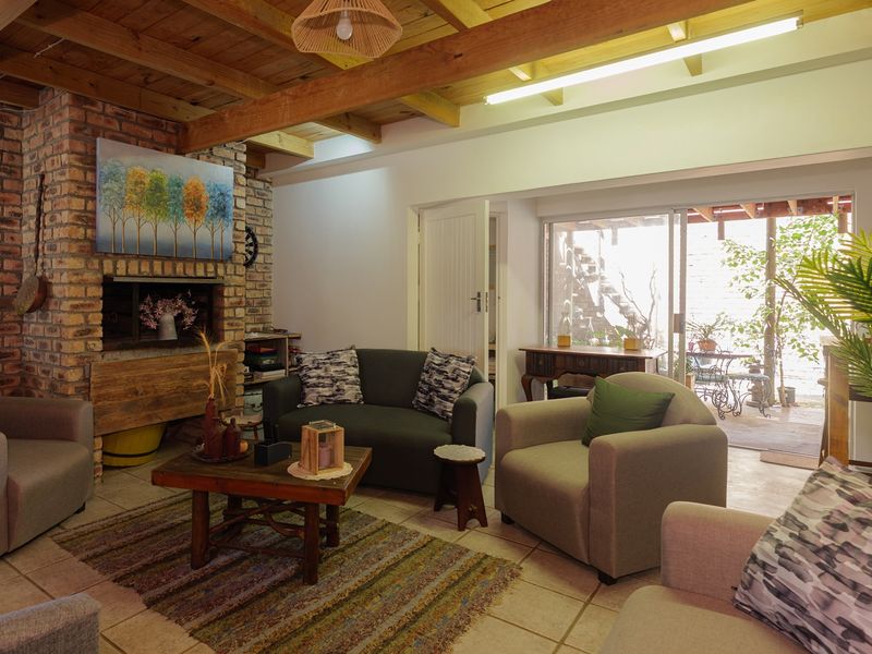 Cozy living room featuring a rustic brick fireplace, exposed timber ceiling beams, and large sliding glass doors providing access to the outdoor patio area.