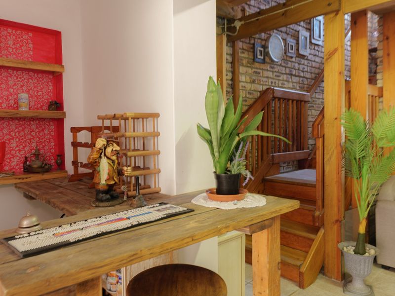 A rustic living area featuring exposed brick walls, a timber staircase with balustrade, and built-in shelving with decorative backing.