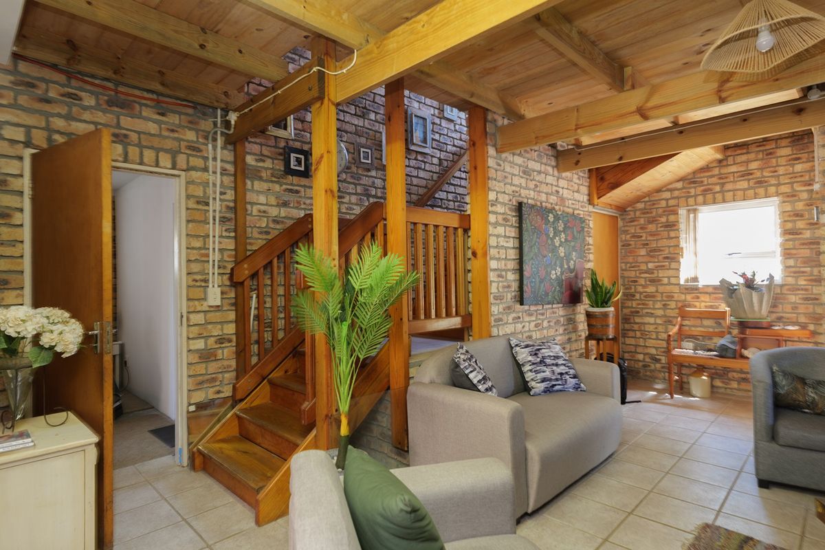 A rustic living room featuring exposed brick walls, timber ceiling beams, and a wooden staircase, creating a warm and character-filled atmosphere.