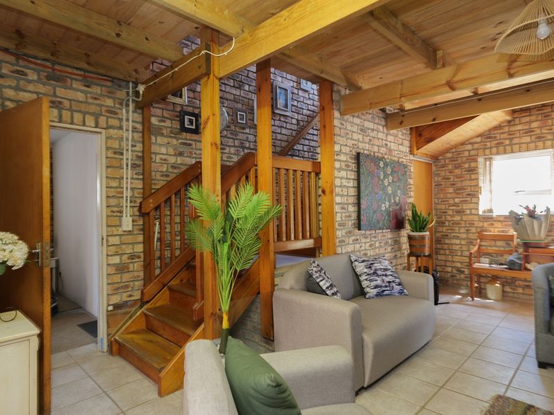 A rustic living room featuring exposed brick walls, timber ceiling beams, and a wooden staircase, creating a warm and character-filled atmosphere.