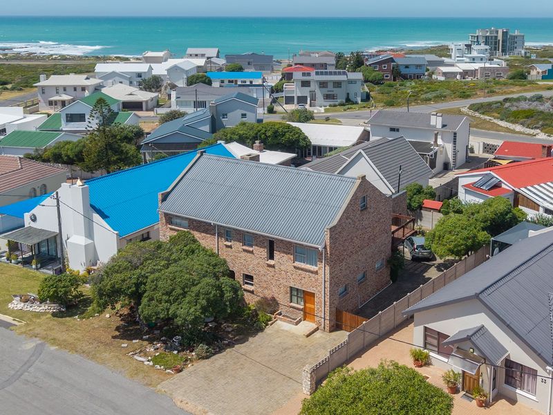 Aerial view of a multi-story brick house with a metal roof, featuring a paved driveway and surrounding residential neighborhood near the coast.