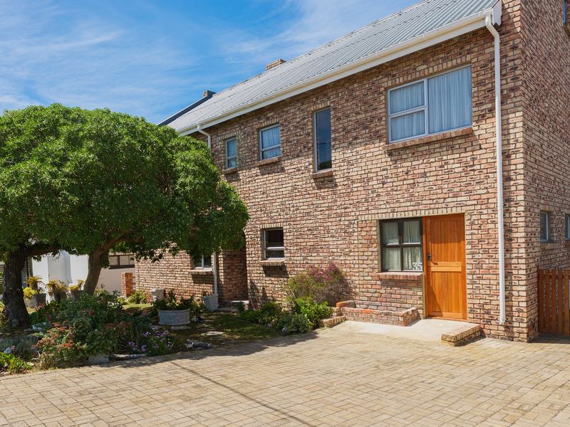 A well-maintained double-storey face brick house featuring a paved driveway, timber entrance door, and established garden area.