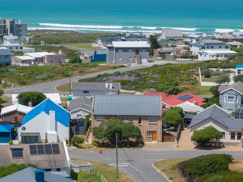 An elevated aerial view of a coastal residential neighborhood featuring various detached houses with pitched roofs and solar panel installations.