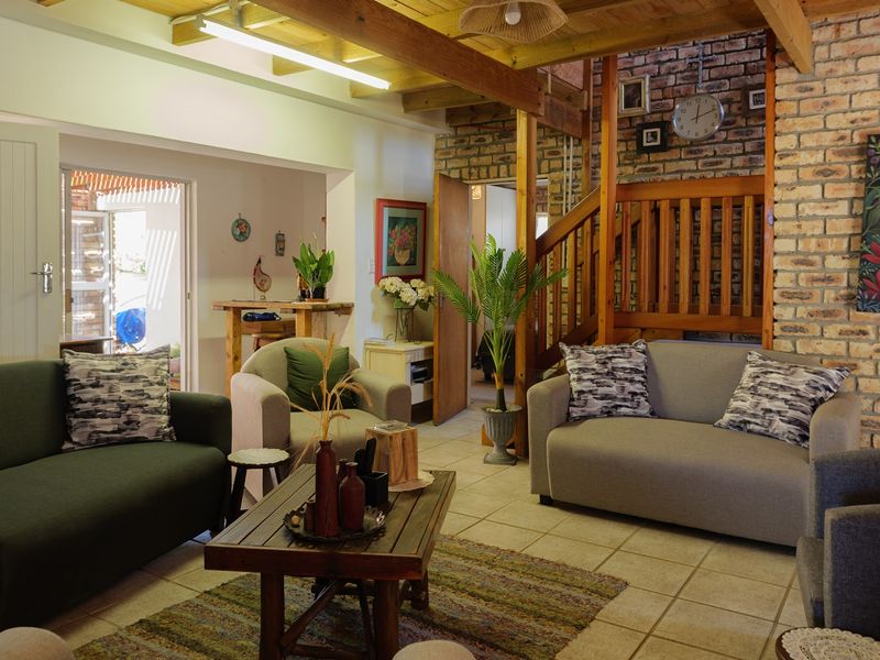 A rustic living room featuring exposed timber ceiling beams, a prominent brick feature wall, and a wooden staircase, creating a warm and textured atmosphere.