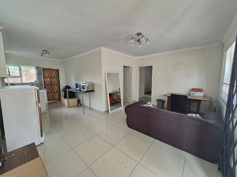 Open-plan living area featuring large format floor tiles, neutral walls, and direct access to the exterior via a security gate.