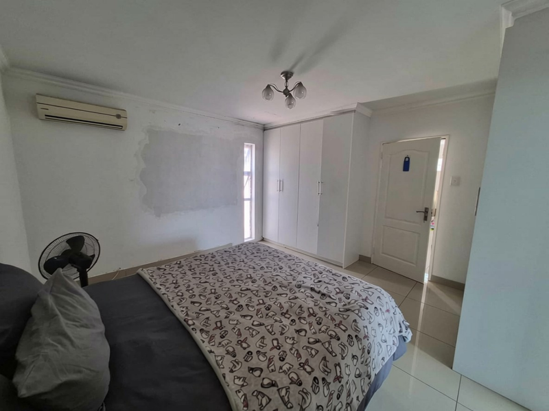 Bedroom featuring tiled flooring, built-in cupboards, and a split-system air conditioner. The walls require cosmetic attention and repainting.