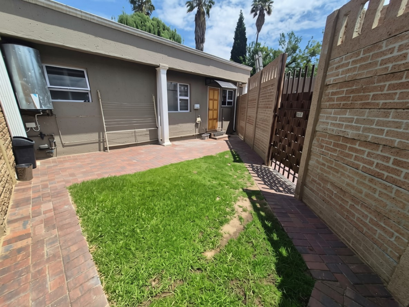A private rear courtyard featuring a paved patio area, a small lawn, and secure brick boundary walls with a metal gate.