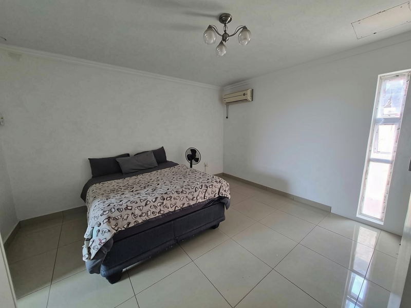 A spacious bedroom featuring neutral tiled flooring, a wall-mounted air conditioning unit, and a central ceiling light fixture.