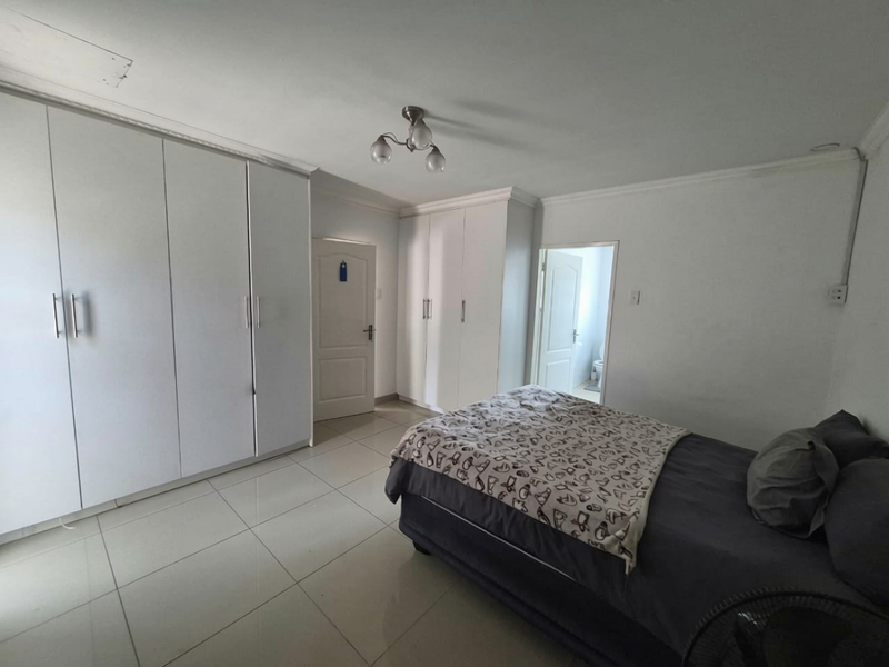 A spacious bedroom featuring extensive built-in cupboards, tiled flooring, and direct access to an en-suite bathroom.