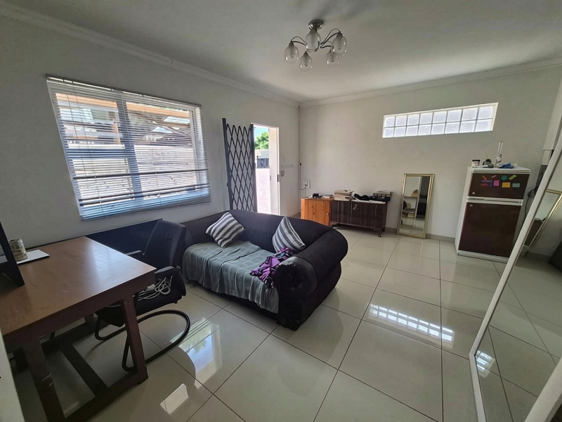 A living area featuring large format floor tiles, a security gate, and a glass block window, providing a functional and bright space.