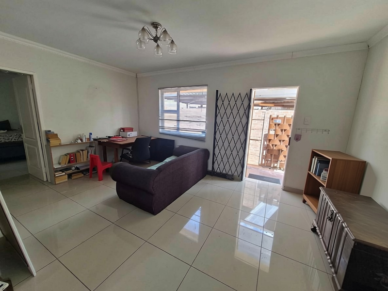 A living room featuring large format floor tiles, a security gate at the entrance, and natural light through the window.