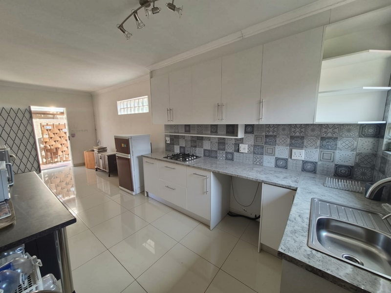 Functional kitchen featuring white cabinetry, patterned tile backsplash, gas hob, and stone-look countertops with direct access to the exterior.