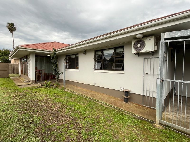 Rear exterior view of the house featuring a concrete pathway, security gates, and an installed air conditioning unit.